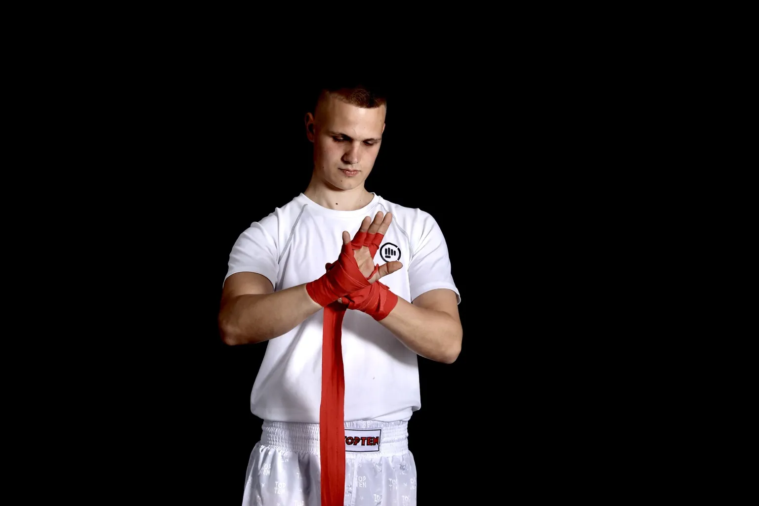 Kickboxer in weißer Trainingskleidung bindet konzentriert rote Handbandagen.