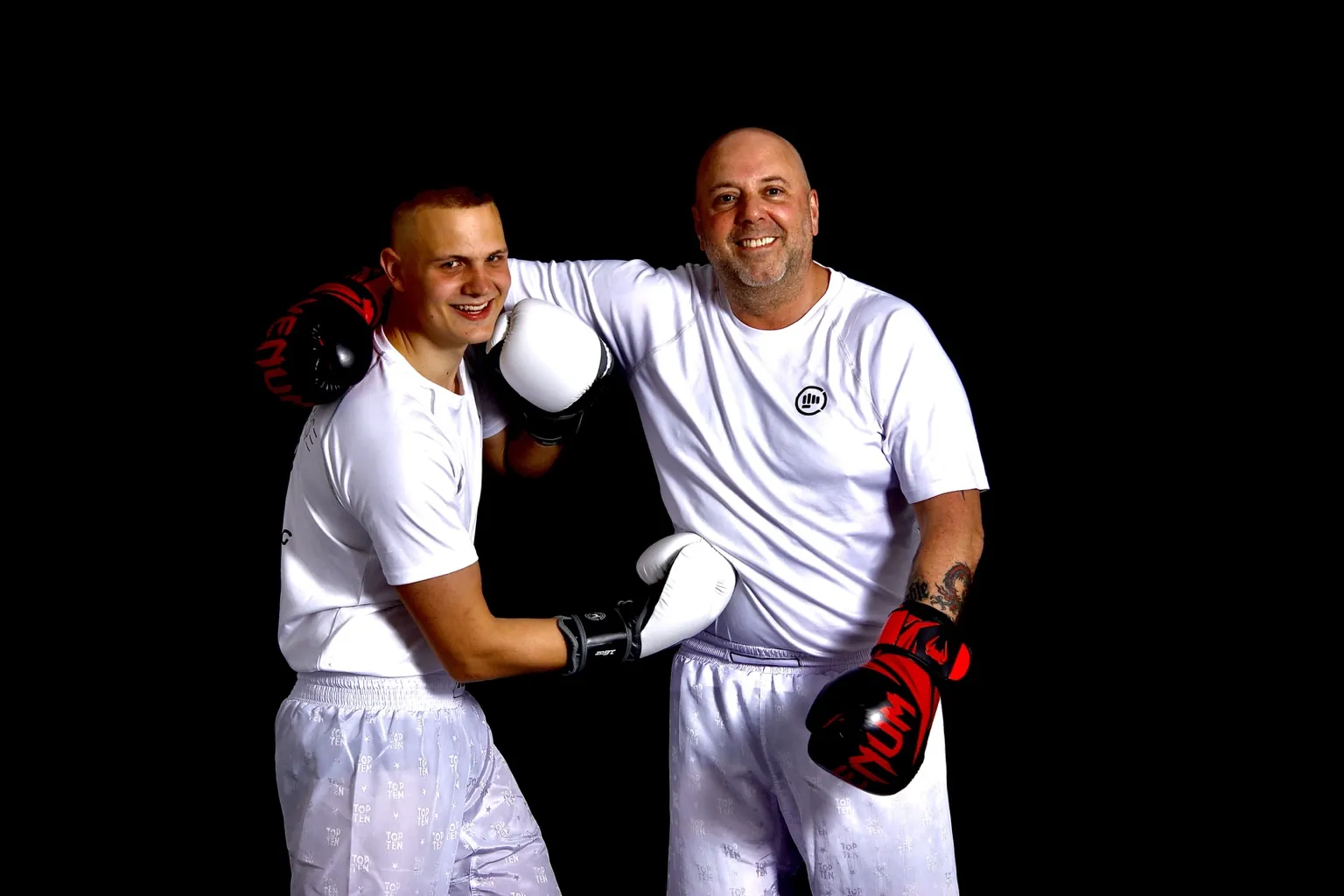 Zwei Erwachsene in weißer Trainingskleidung lachen gemeinsam mit Boxhandschuhen.