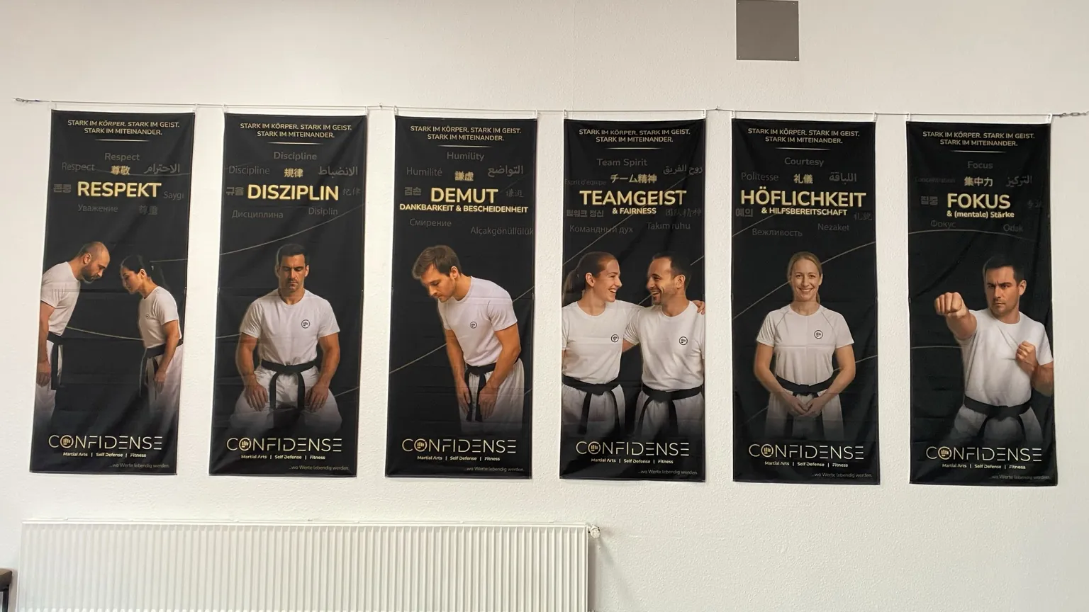 Sechs Werteposter mit Respekt, Disziplin, Demut, Teamgeist, Höflichkeit und Fokus hängen im CONFIDENSE-Studio.