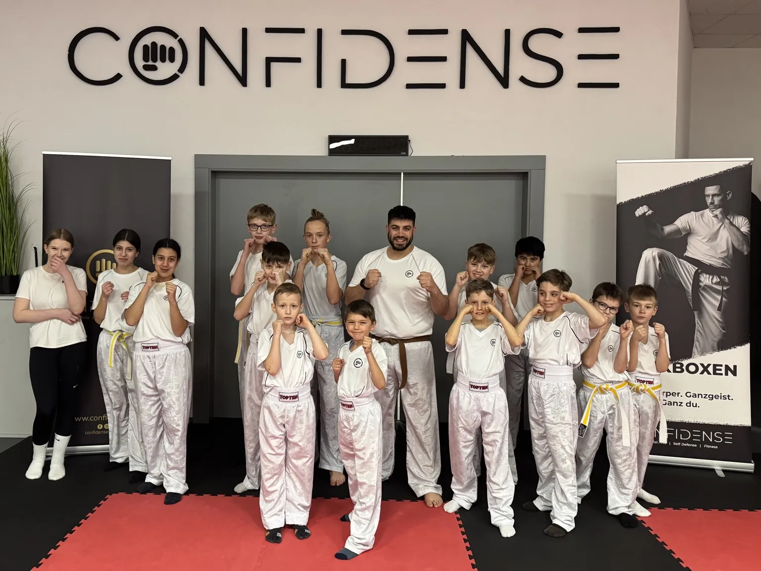 Große Kinder- und Jugendgruppe steht gemeinsam in Trainingskleidung im CONFIDENSE-Studio.