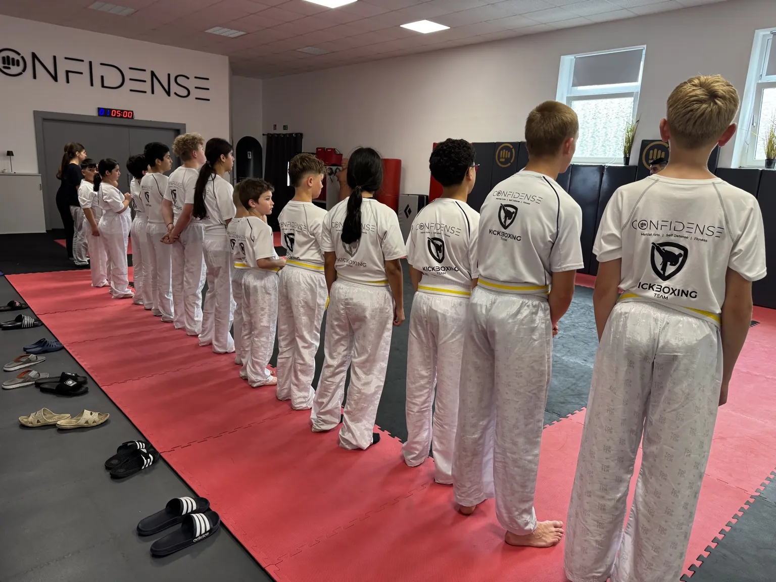 Kinder und Jugendliche stehen in einer Reihe auf der Trainingsfläche des CONFIDENSE-Studios und warten auf die nächste Übung.