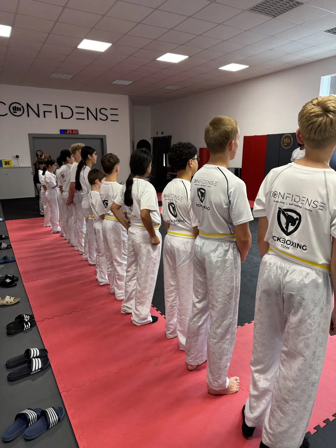 Kinder und Jugendliche stehen aus seitlicher Perspektive in einer Reihe im CONFIDENSE-Kickboxtraining.