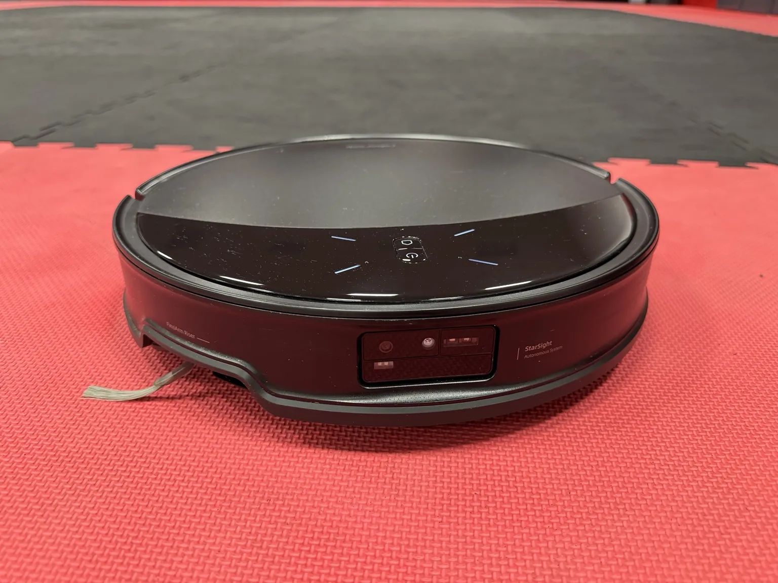 Ein automatischer Saug- und Wischroboter steht auf der roten Trainingsmatte im CONFIDENSE-Studio.