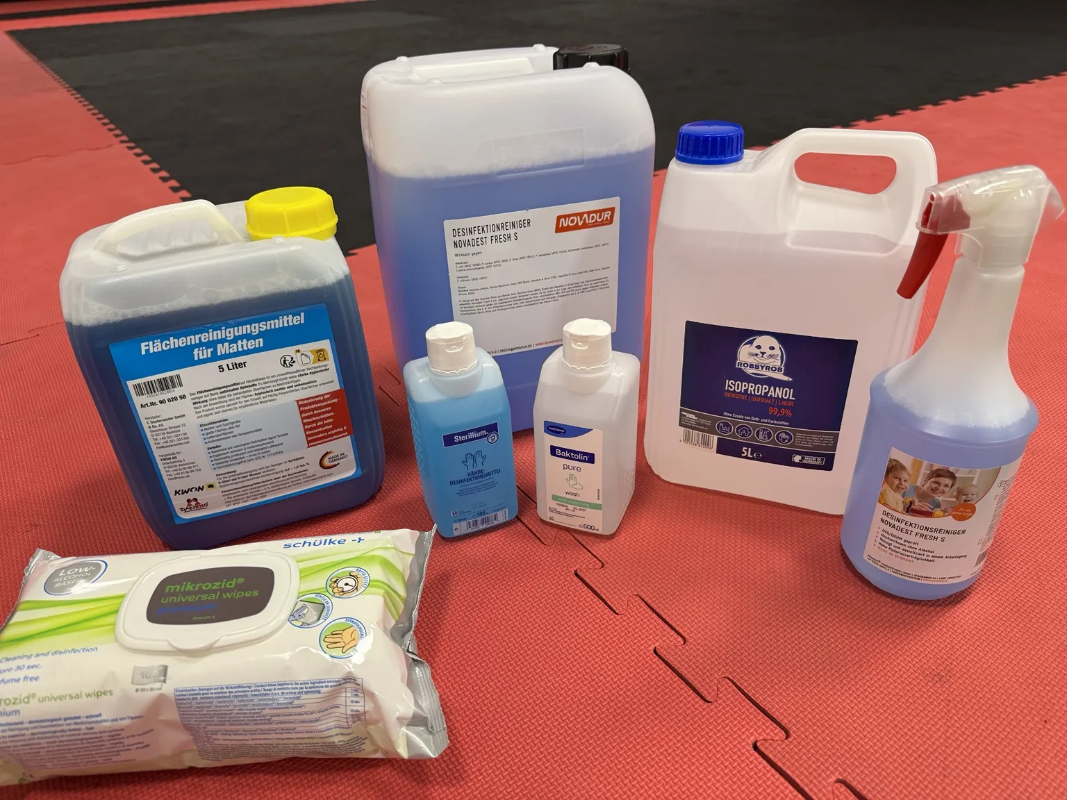 Auswahl verschiedener Reinigungs-, Desinfektions- und Hygieneprodukte auf der Trainingsmatte des CONFIDENSE-Studios.